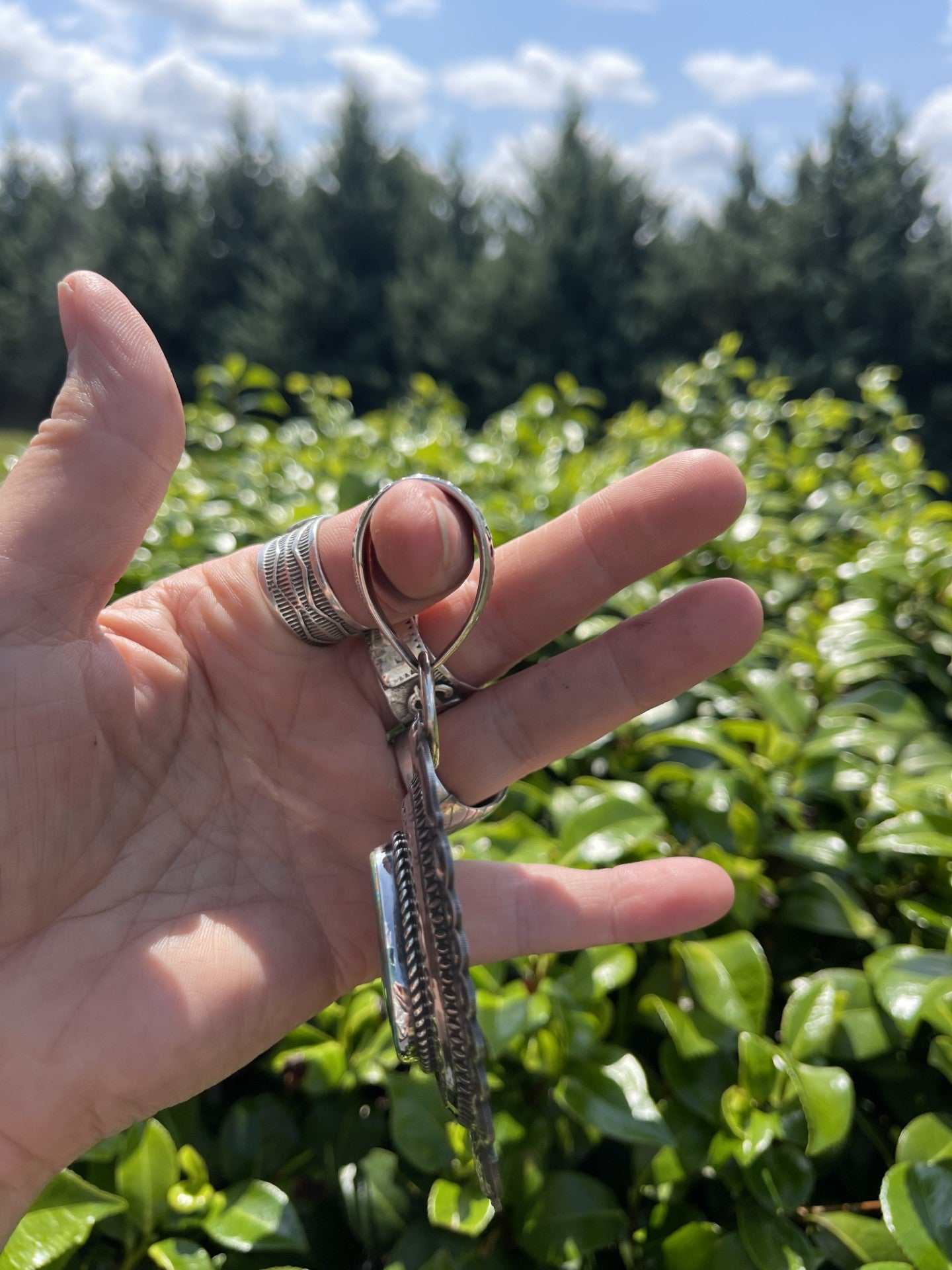 Hand holding Native American Pilot Mountain Turquoise Pendant with detailed silverwork and turquoise stone against green foliage background outdoors
