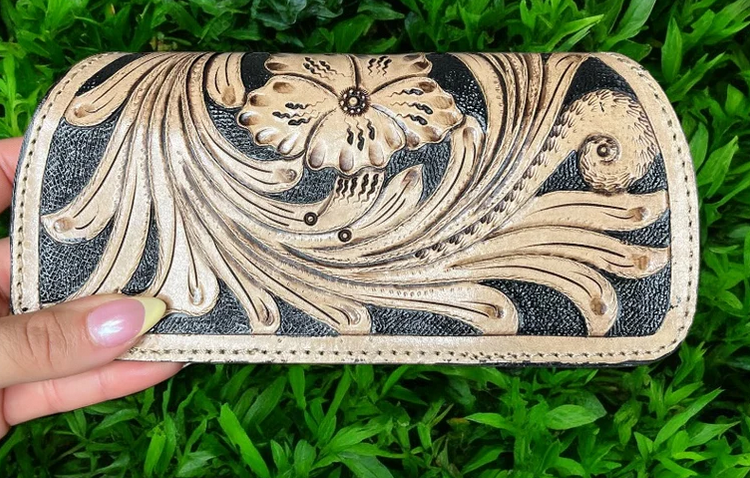 Brown cowhide tooled floral design sunglasses case held above green grass background