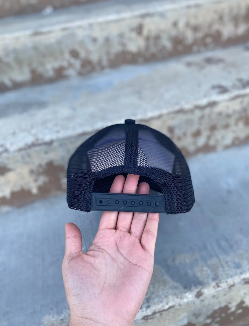 Back view of a black mesh cap with adjustable strap, held in a hand.
