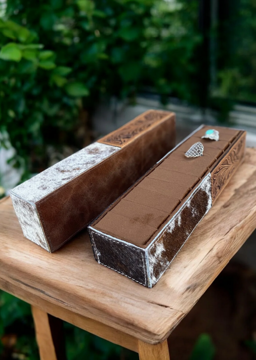 Cowhide and tooled leather ring holder on wooden table.