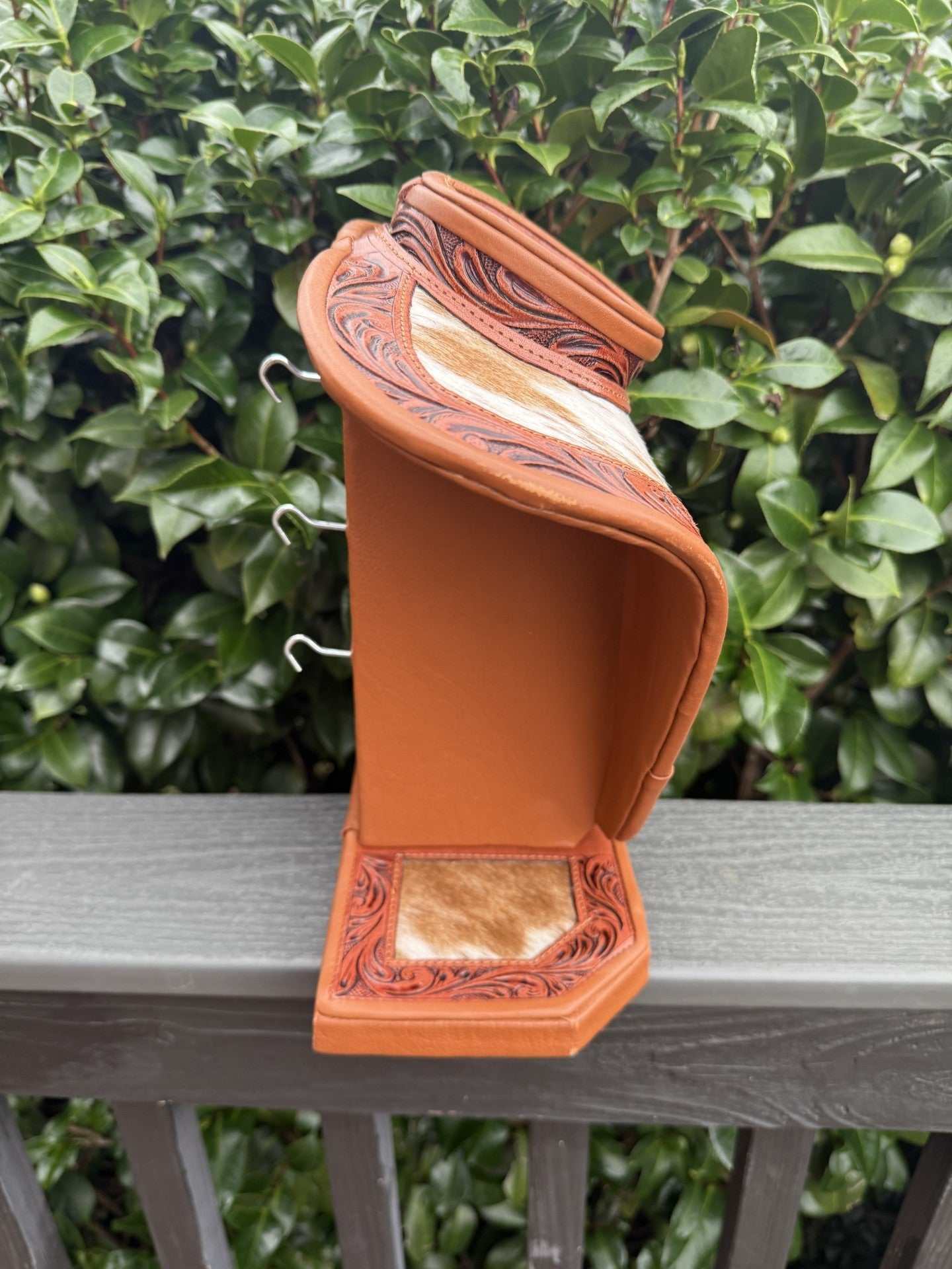 Tan tooled leather and cowhide necklace display with decorative patterns and hooks for jewelry organization