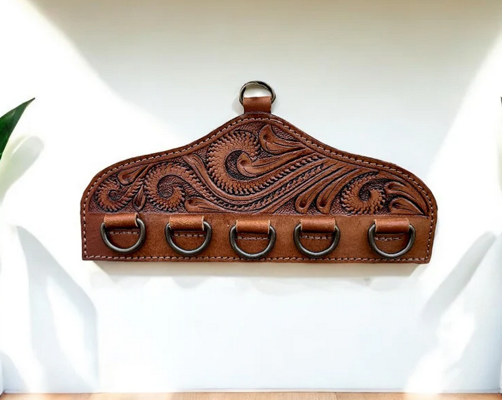 Tooled leather scarf display with decorative floral pattern and five metal rings for hanging scarves