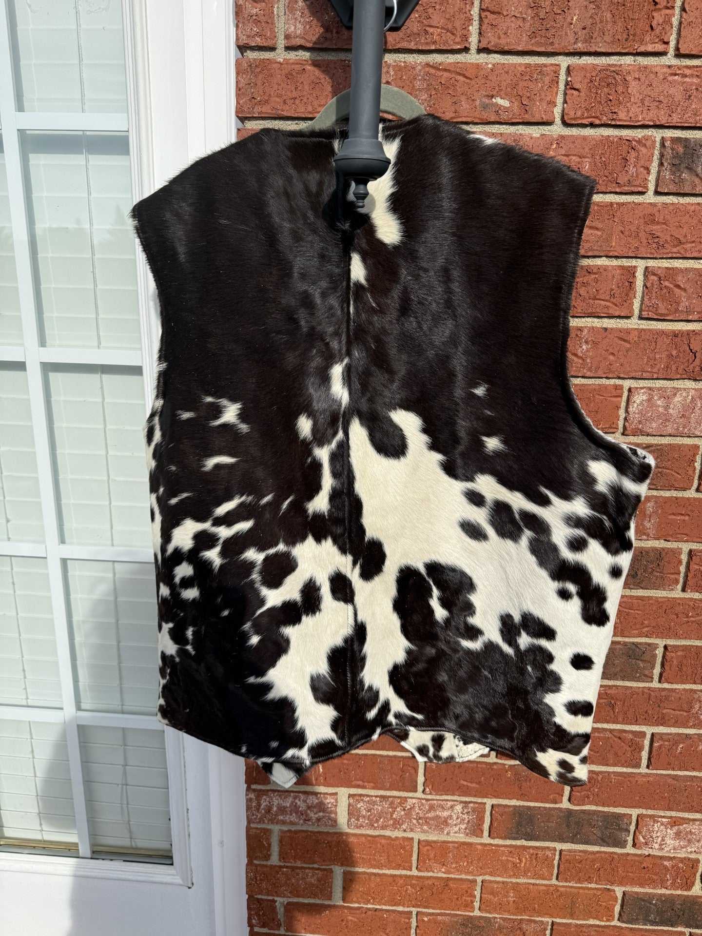 Cowhide men’s vest 2XL Western leather sleeveless jacket in black and white pattern hanging on brick wall