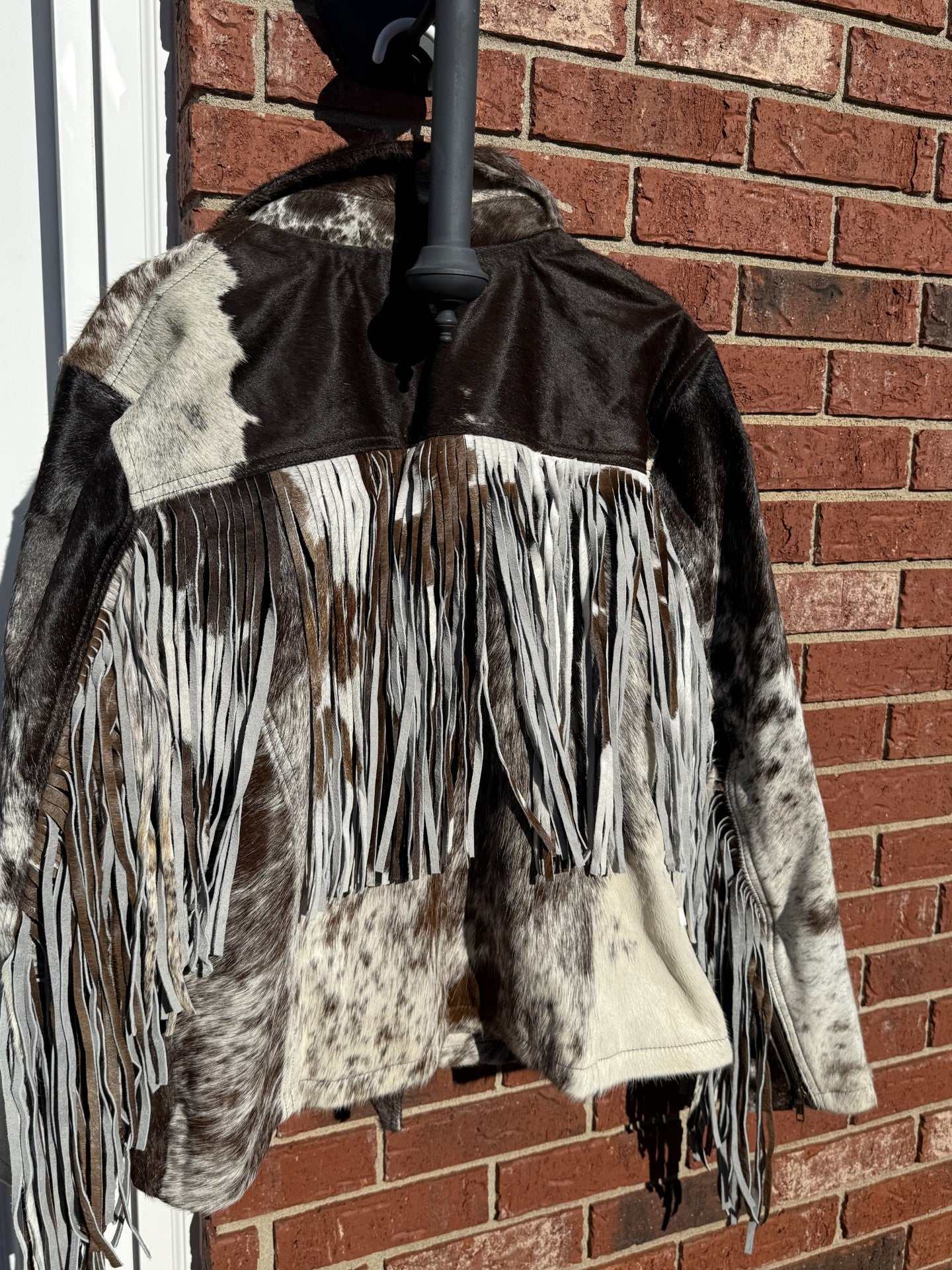 Medium size brown cowhide leather jacket with fringe detail hanging against a brick wall