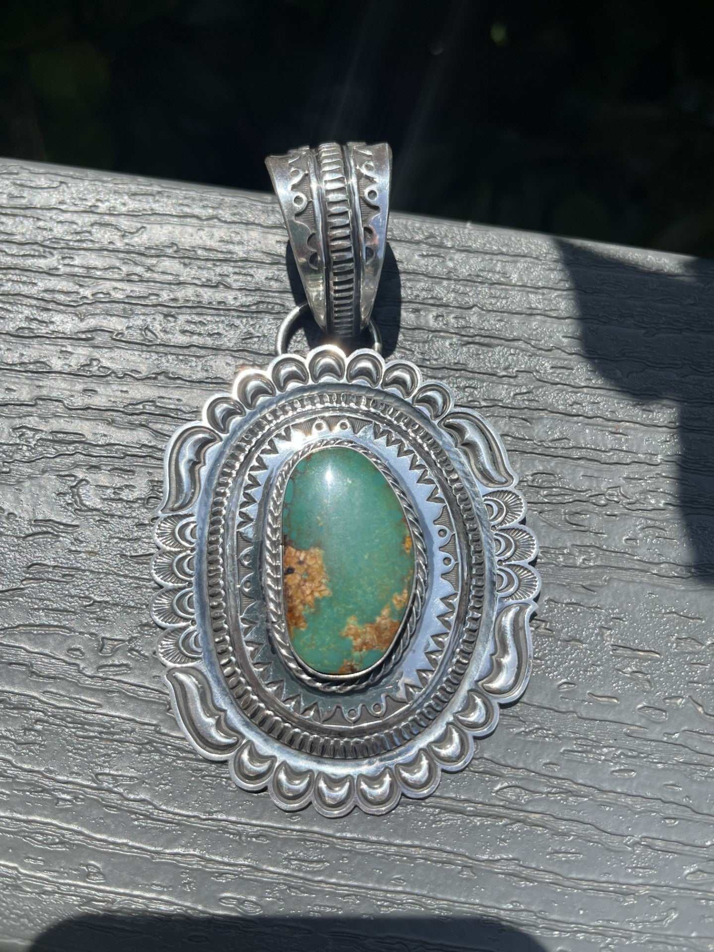 Native American green Pilot Mountain turquoise pendant with intricate silver setting and ornate bail.