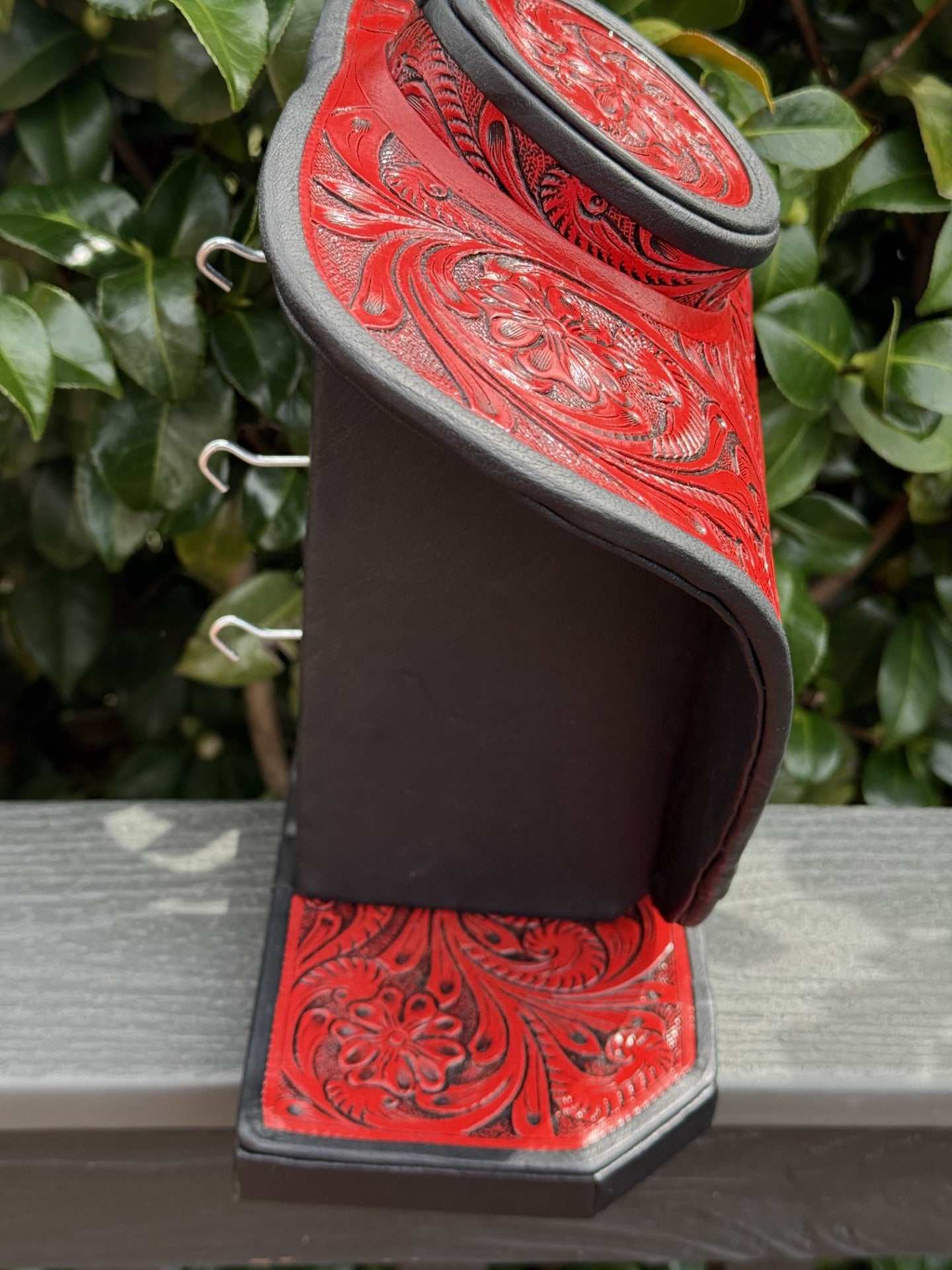 Red and brown all tooled leather necklace display with intricate floral patterns and hooks for jewelry organization