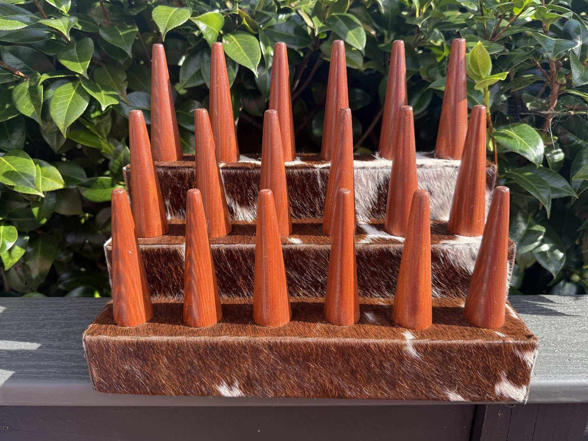 18 Finger Cowhide ring holder in brown-and-white spotted hide with polished wooden pegs and a matching base