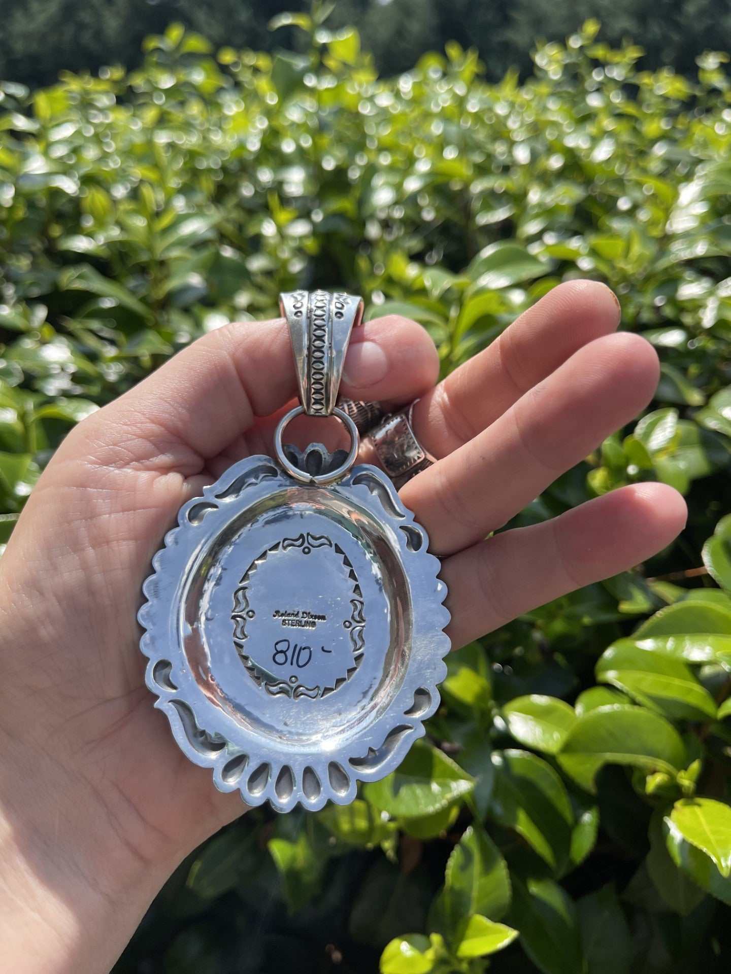 Back view of Native American Pilot Mountain Turquoise Pendant by Roland Dixson held in hand against green foliage background