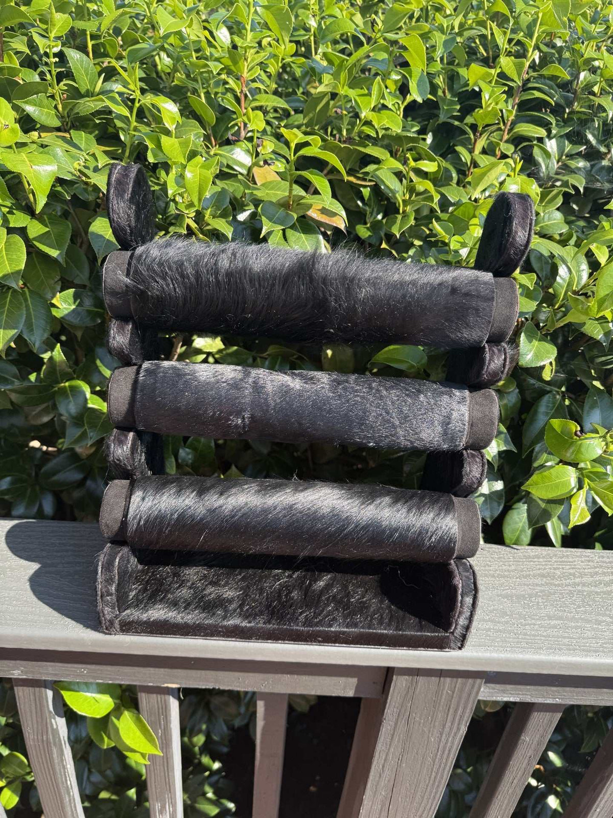 Black Cowhide bracelet display with four horizontal cushioned bars covered in black cowhide fur, rustic and durable design