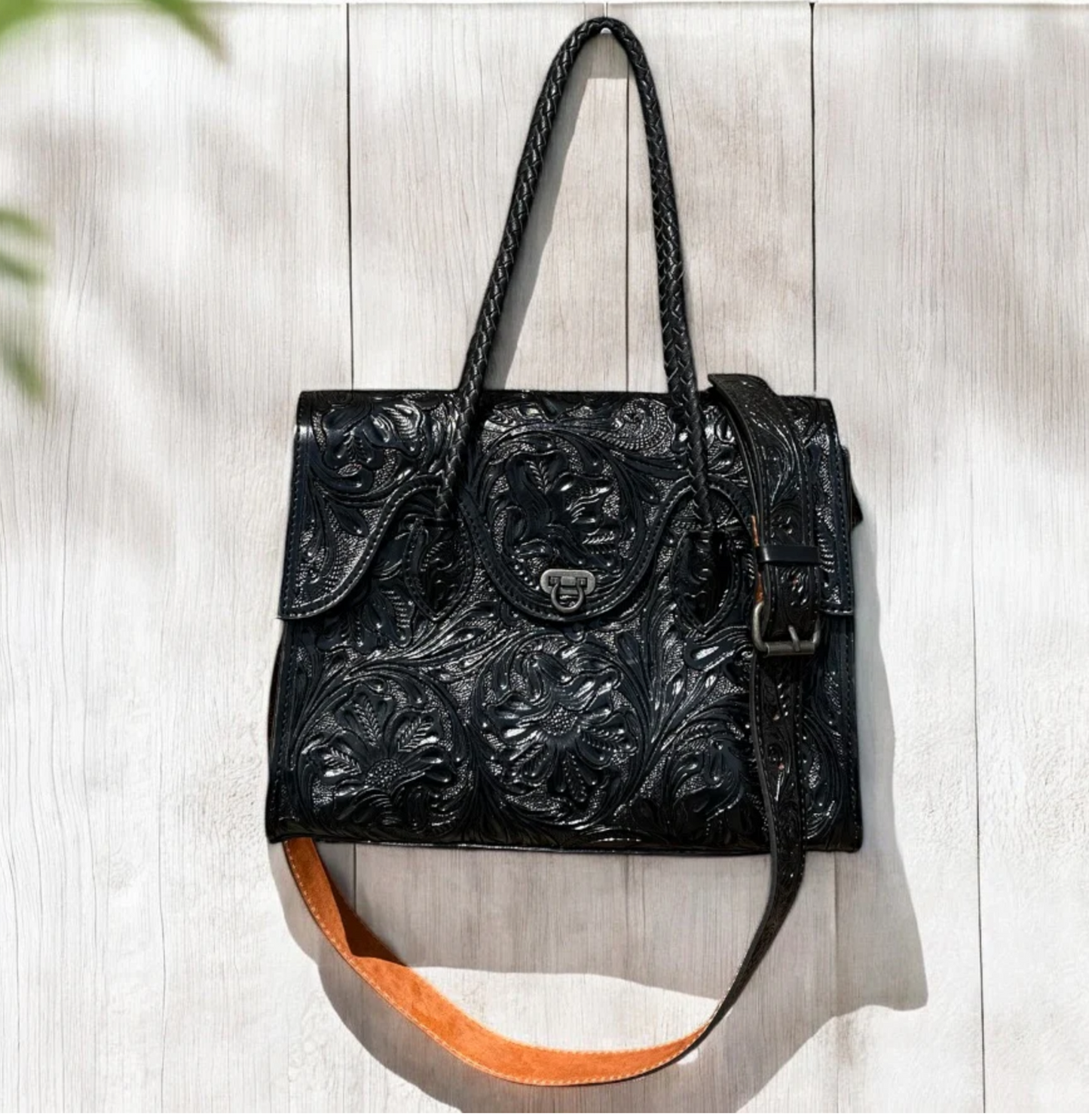 Black hand tooled crossbody purse with adjustable strap and multiple compartments.