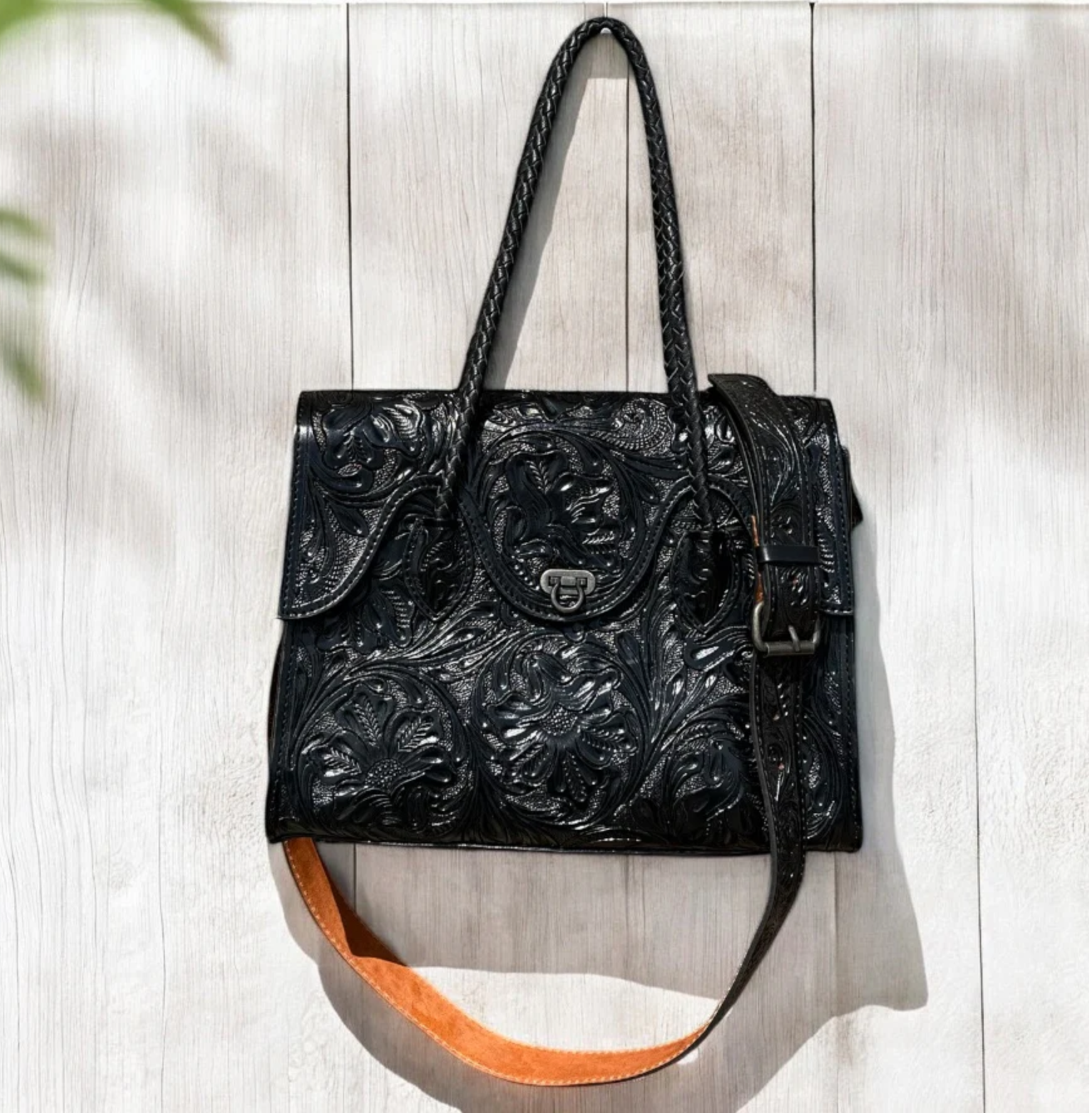 Black hand tooled crossbody purse with adjustable strap and multiple compartments.