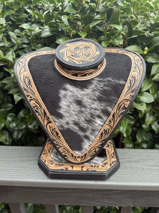 Black and brown tooled leather and black and white cowhide necklace display on outdoor background
