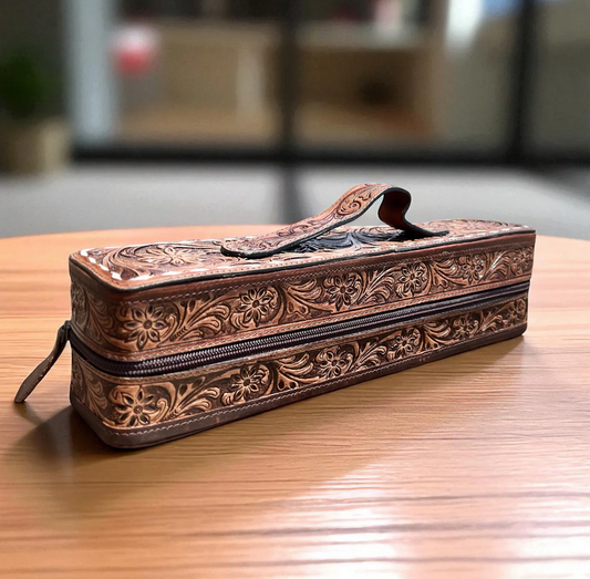 Tan and cowhide leather bracelet-cuff box with floral embossed design and zipper closure on wooden surface