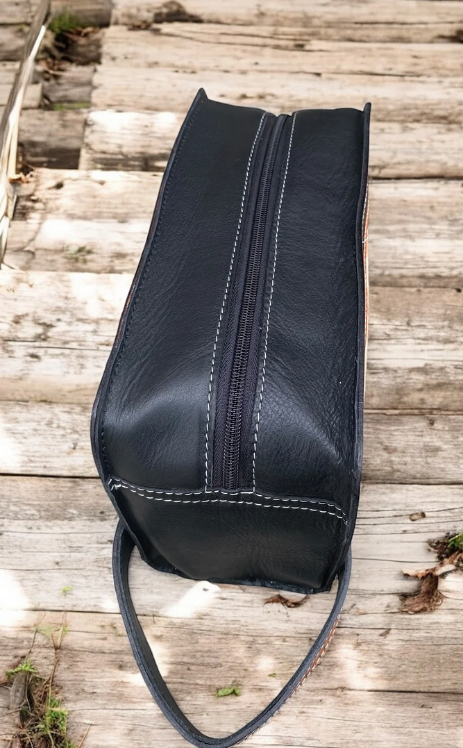 Cowhide and tooled leather toiletry bag with zipper closure on wooden background.