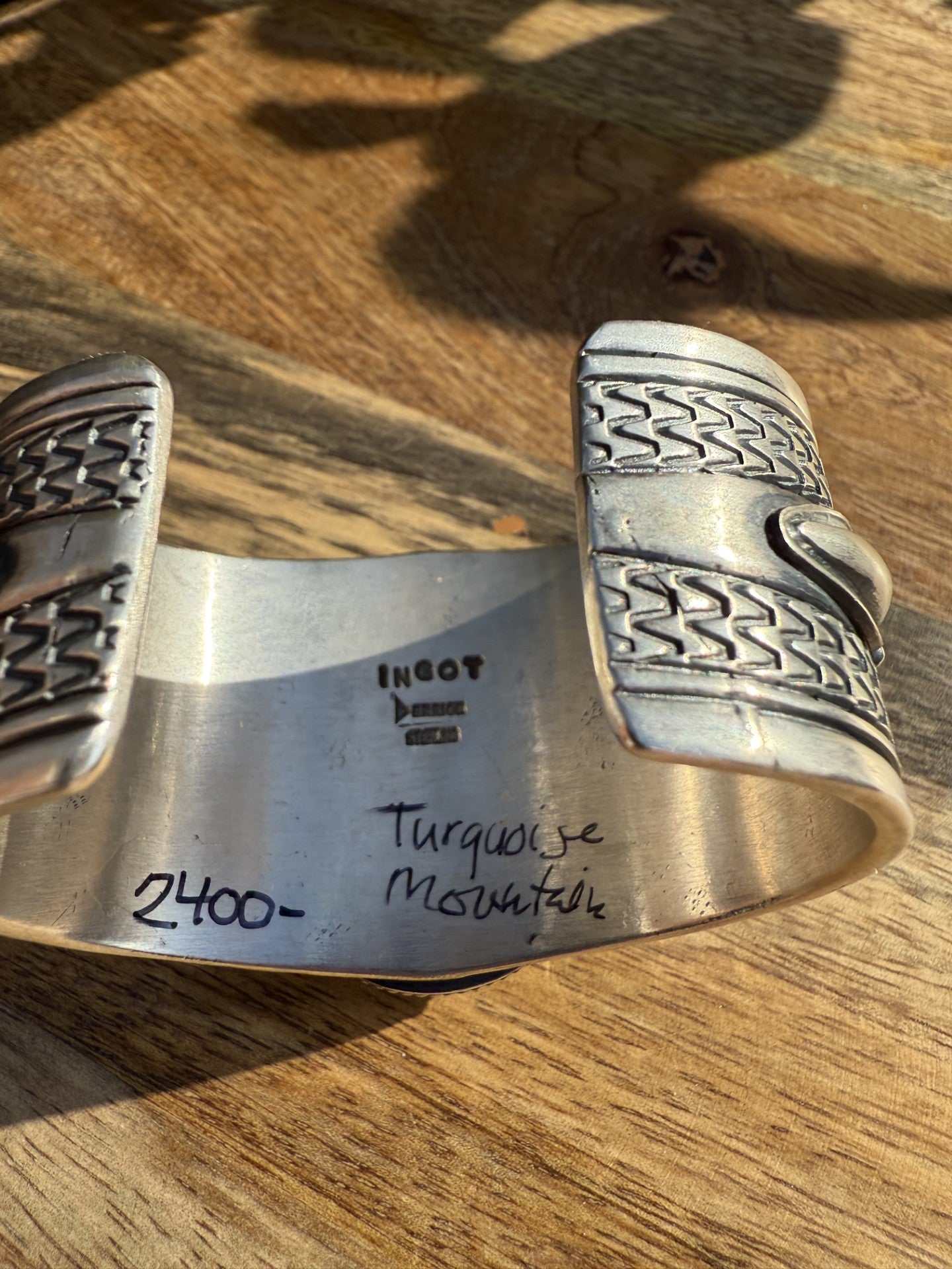 Turquoise Mountain Cuff by Derrick Gordon made of ingot silver with intricate patterns on wooden surface
