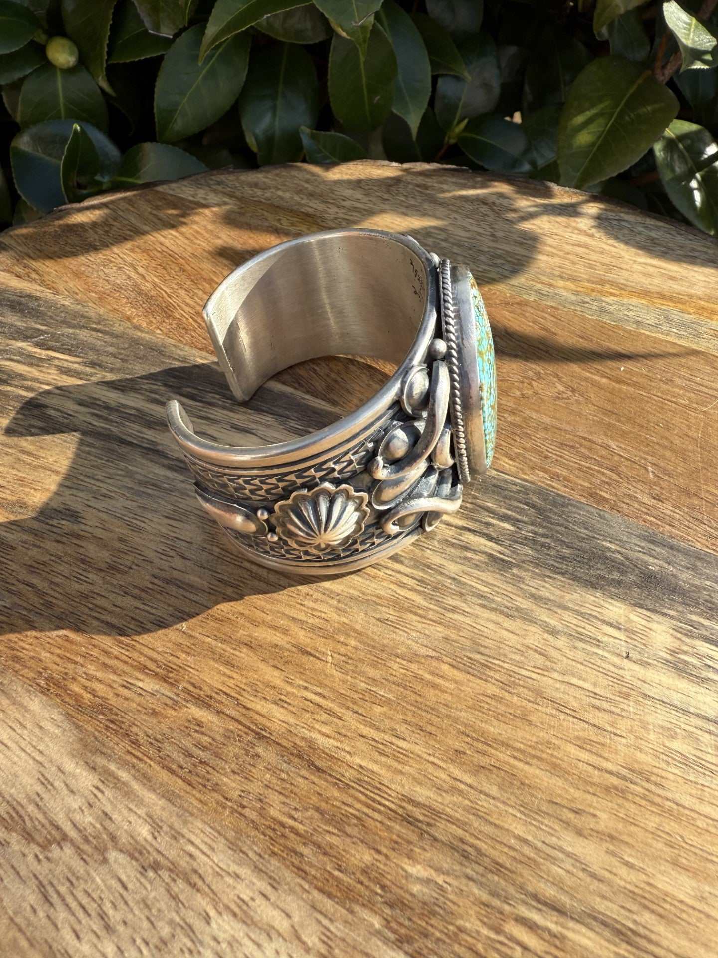 Turquoise Mountain Cuff by Derrick Gordon made of ingot silver with intricate Navajo design on wooden surface