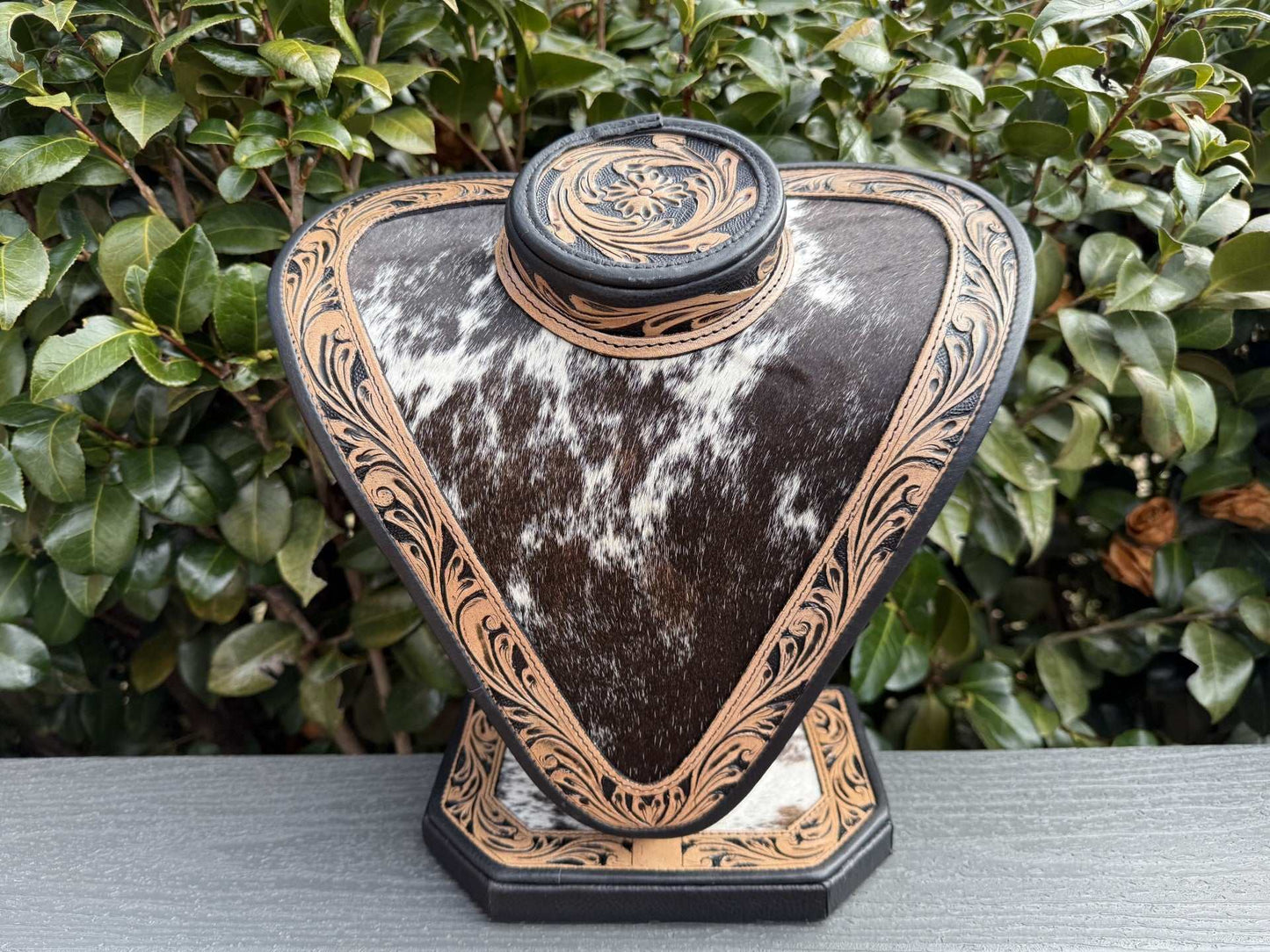 Necklace display with dark and light brown tooled leather and black and white cowhide showcasing jewelry