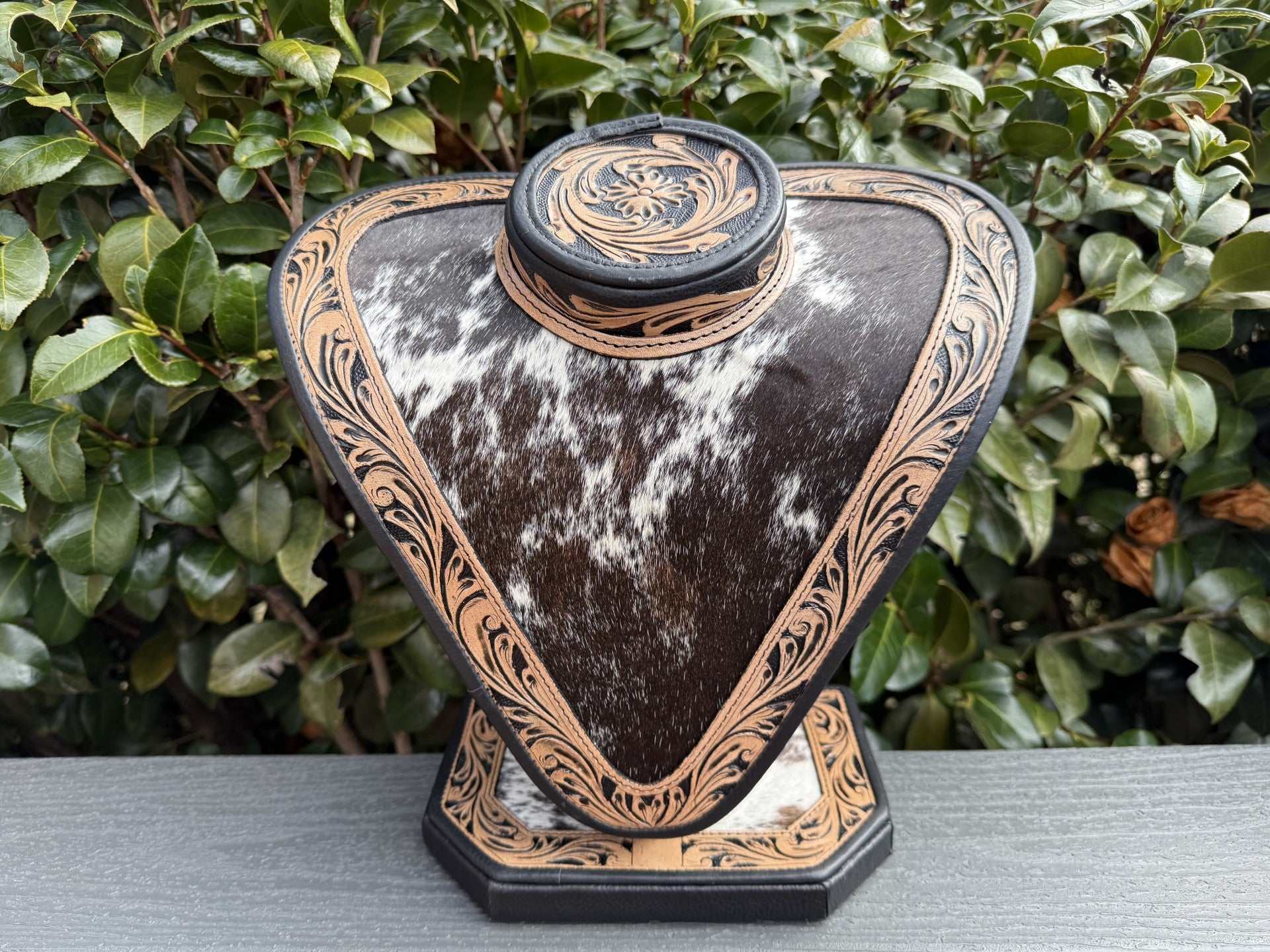 Necklace display with dark and light brown tooled leather and black and white cowhide showcasing jewelry