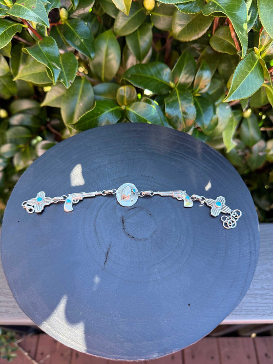 Robby Manuelito Bracelet with turquoise and Western-themed sterling silver charms on black display against green leaves