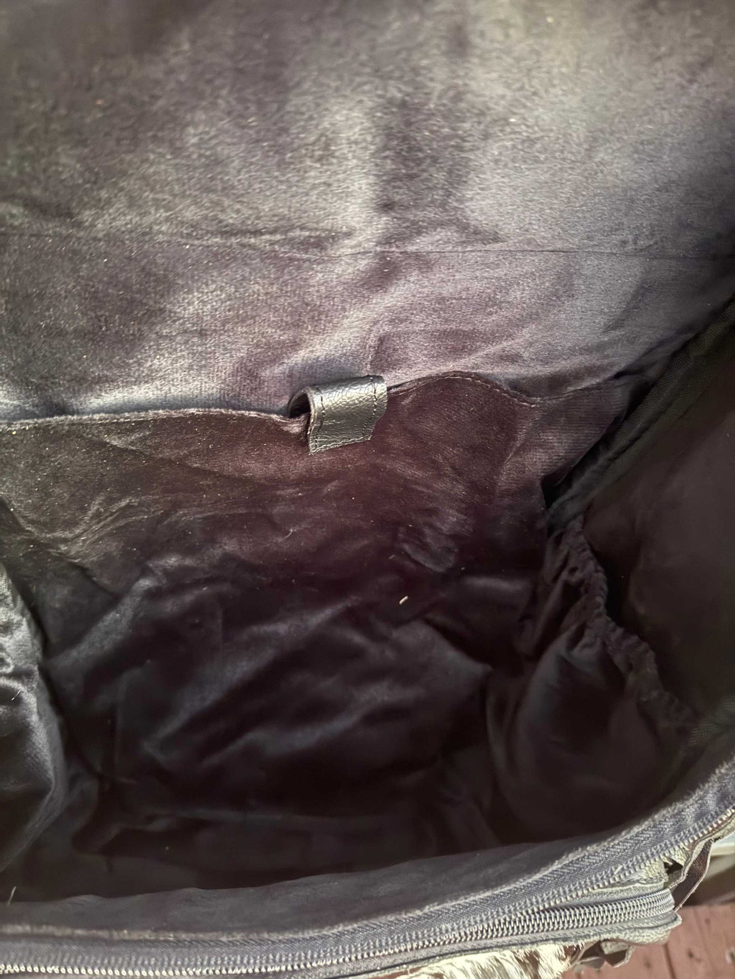 Interior view of black tooled leather and cowhide fringe backpack showing soft lining and zipper pocket