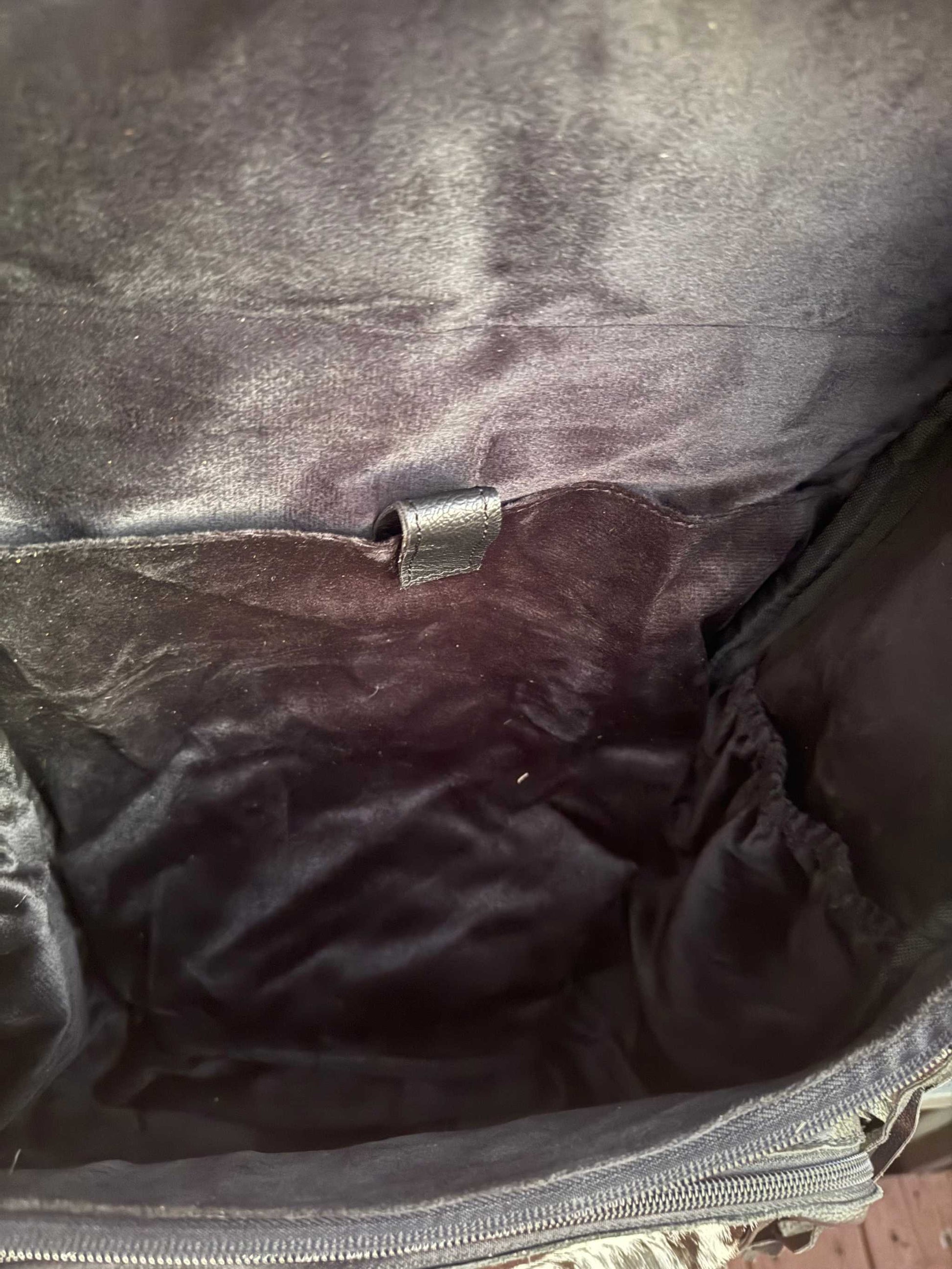 Interior view of black tooled leather and cowhide fringe backpack showing soft lining and zipper pocket