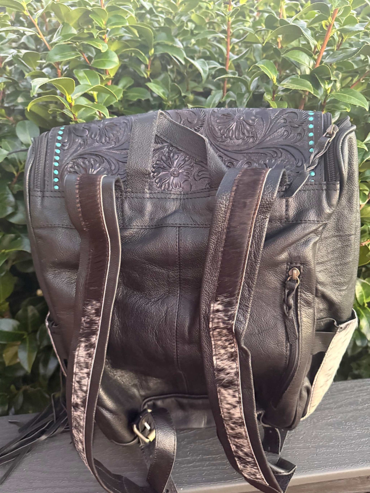 Black tooled leather and cowhide fringe backpack with detailed floral patterns and adjustable straps