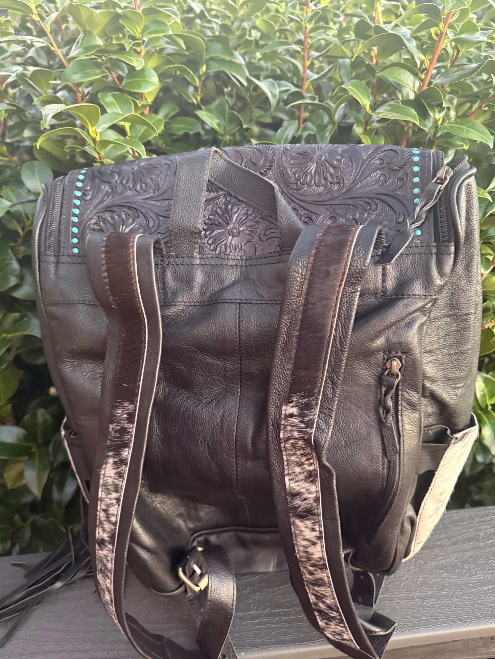 Black tooled leather and cowhide fringe backpack with detailed floral patterns and adjustable straps