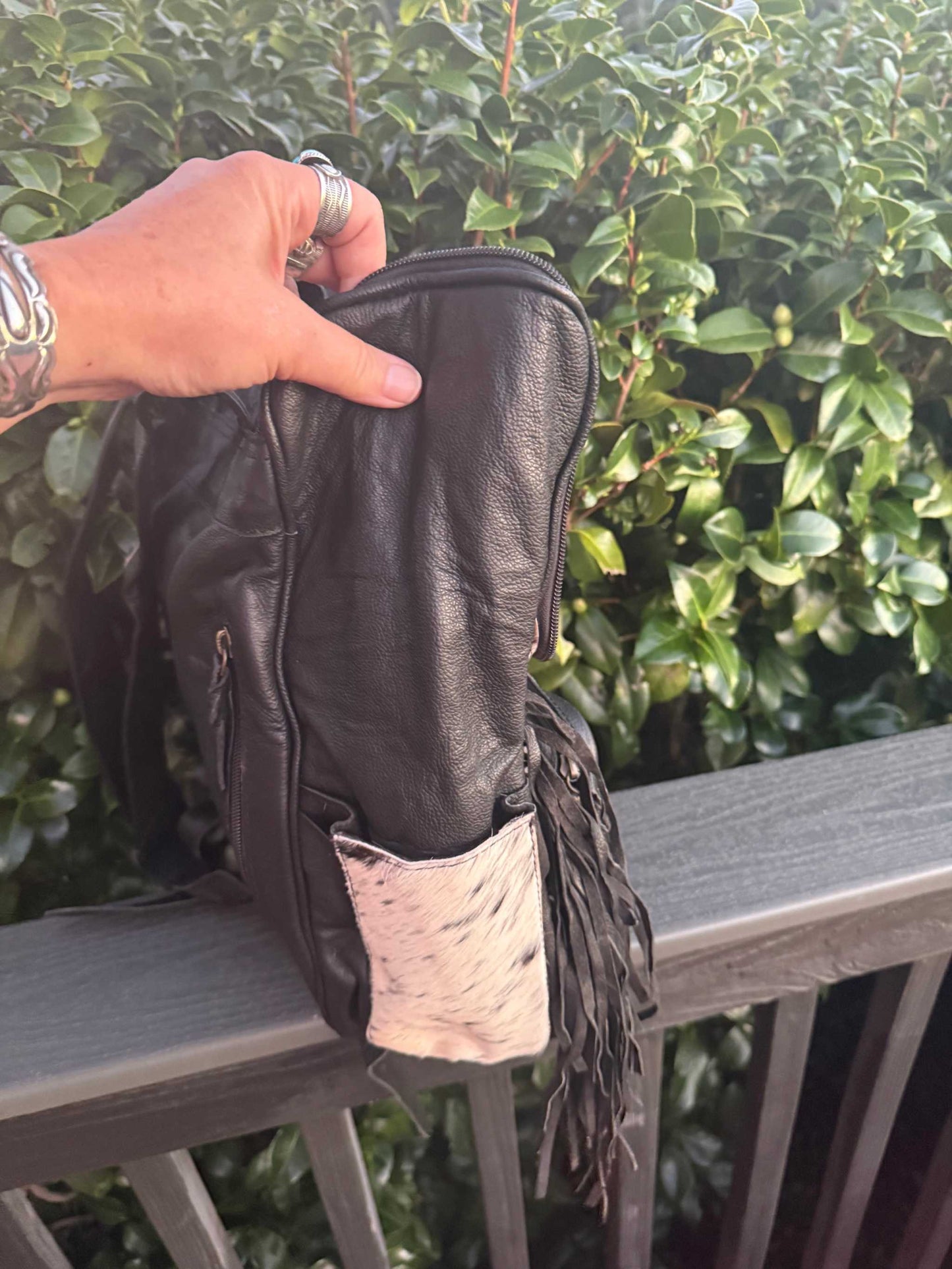 Black tooled leather and cowhide fringe backpack held outdoors by hand