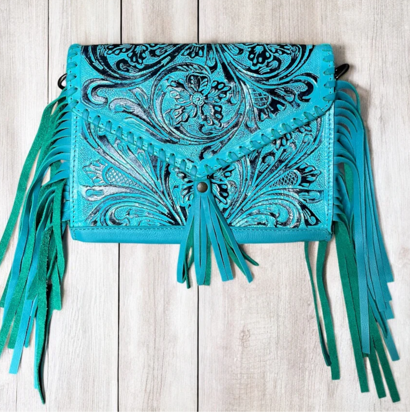 Turquoise hand tooled crossbody bag with fringe detailing and adjustable strap.