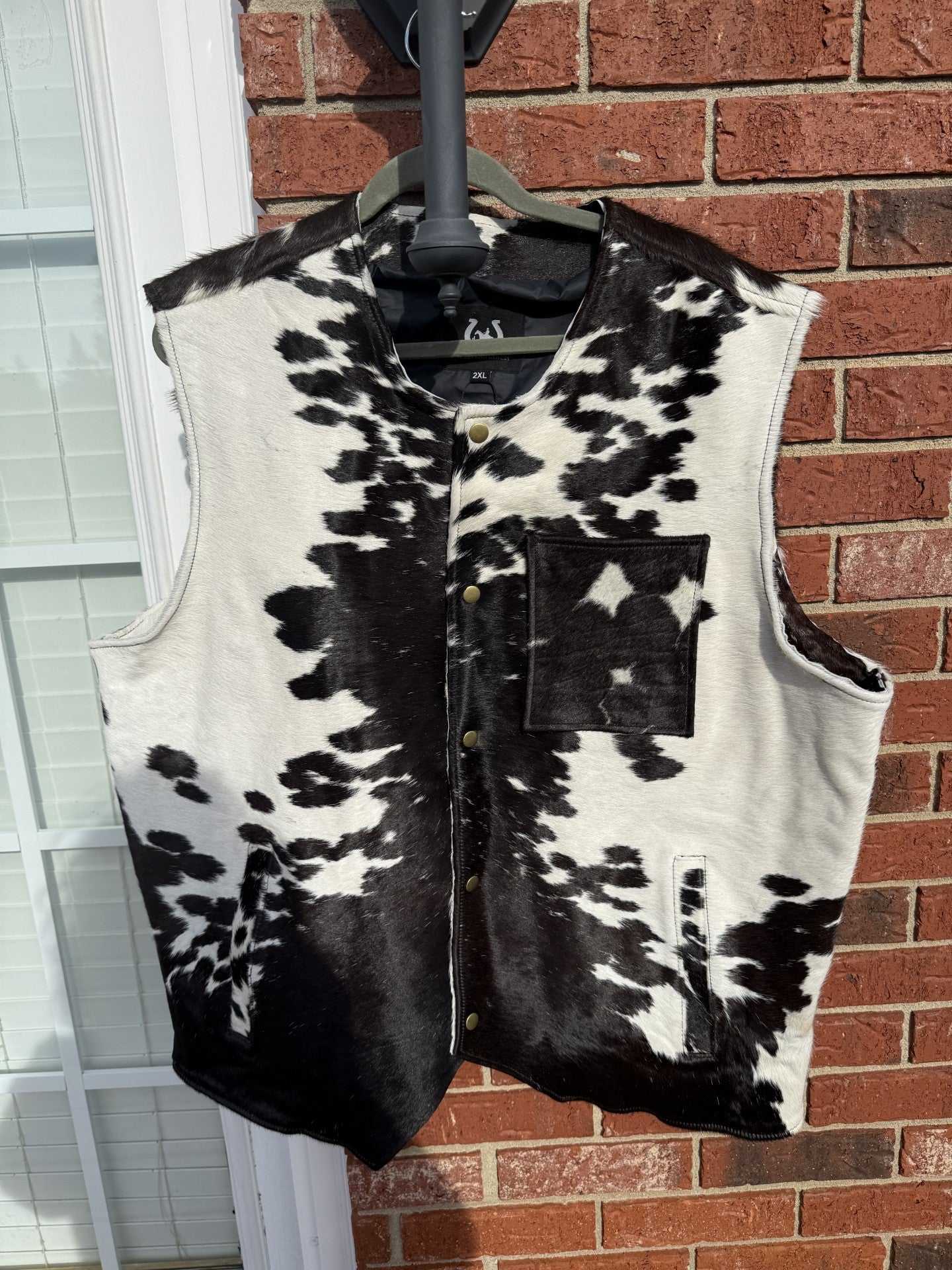 Black and white cowhide men’s vest size 2XL hanging against brick wall