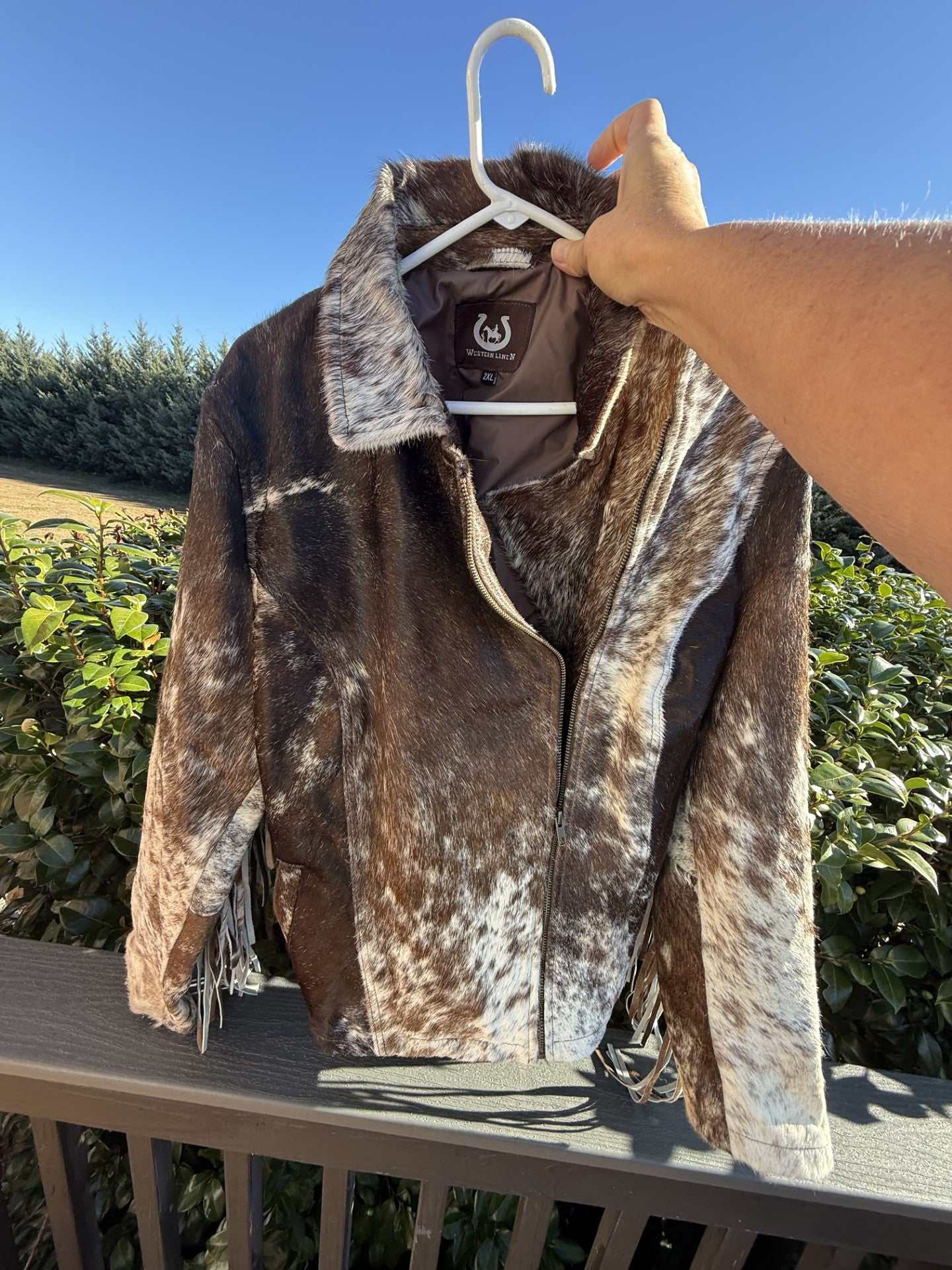 Brown cowhide jacket with fringe in 2XL size hanging outdoors