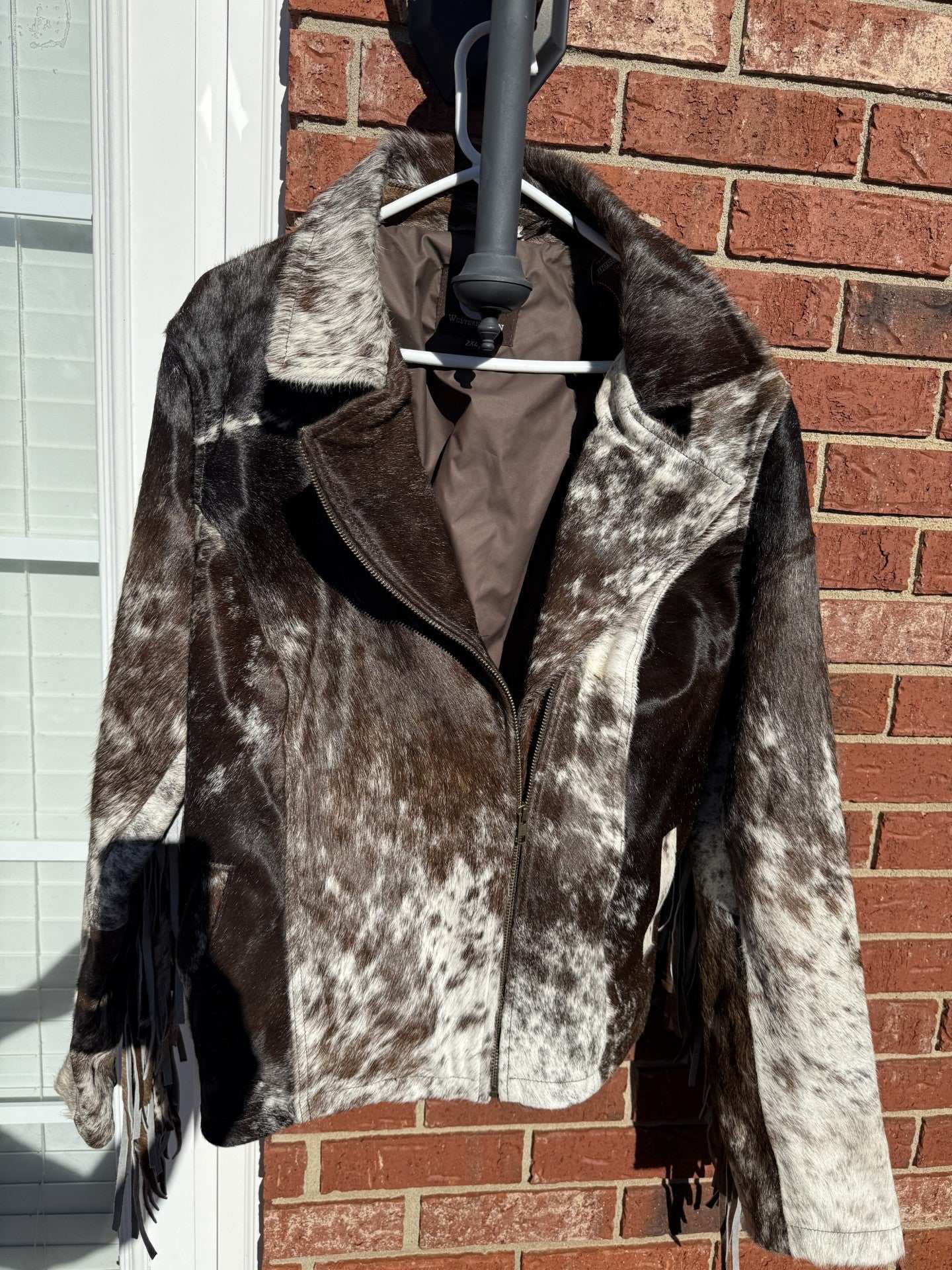 Brown cowhide leather jacket with fringe in medium size hanging outdoors