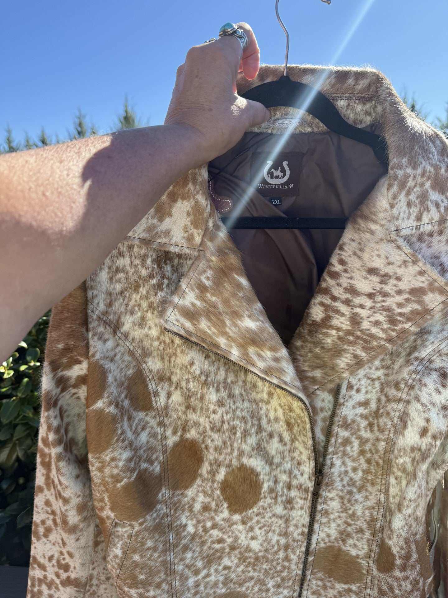 Tan cowhide jacket with unique brown and white spots in size 2XL displayed on hanger outdoors