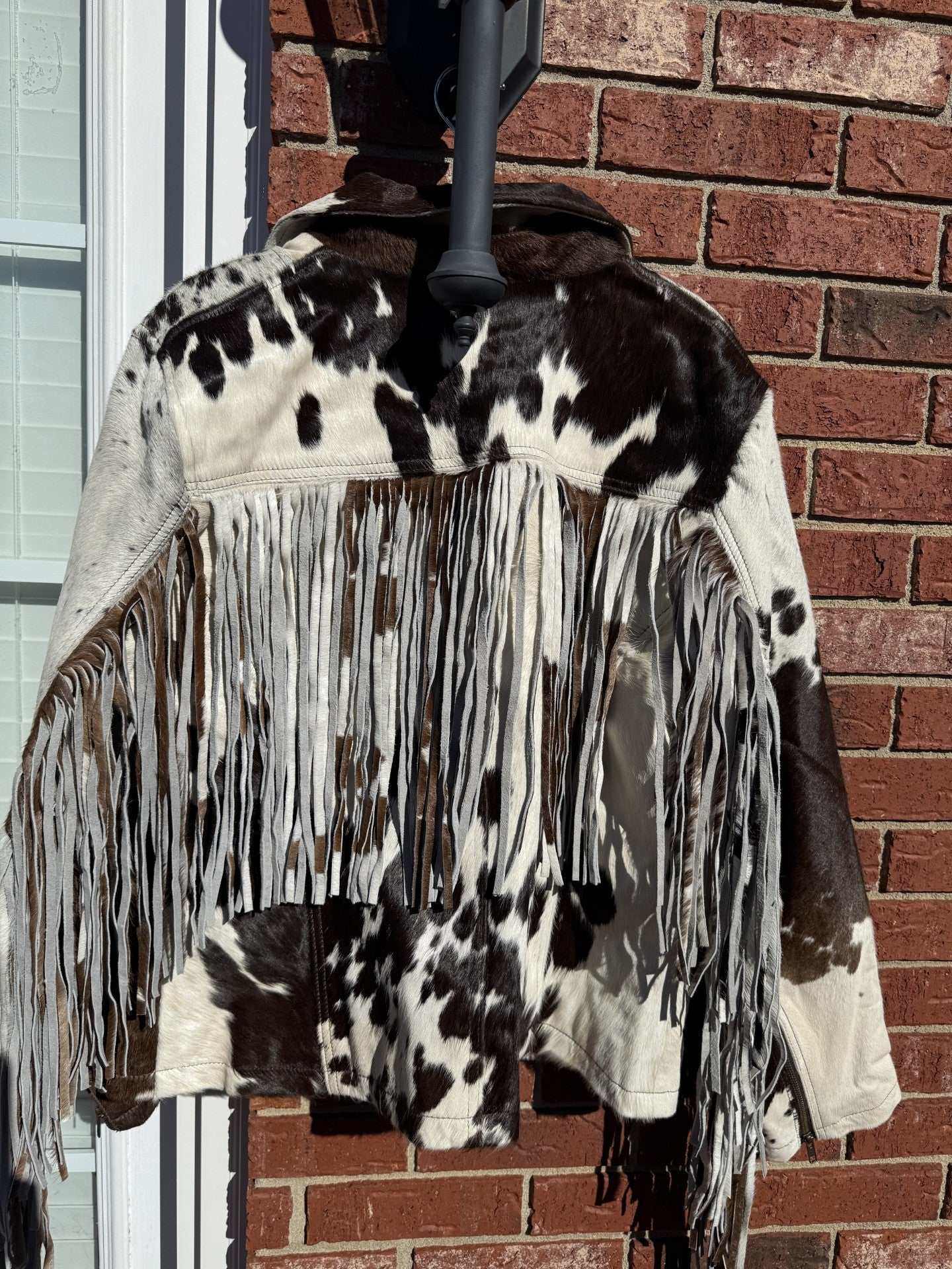 Brown cowhide jacket with fringe in 2XL size hanging outdoors against a brick wall