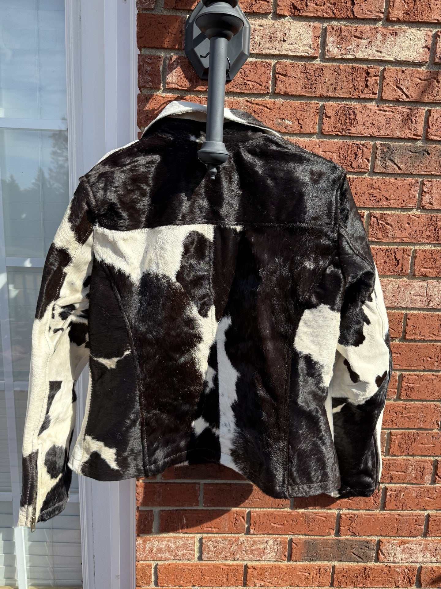 Back view of XL black and white cowhide leather jacket hanging on brick wall