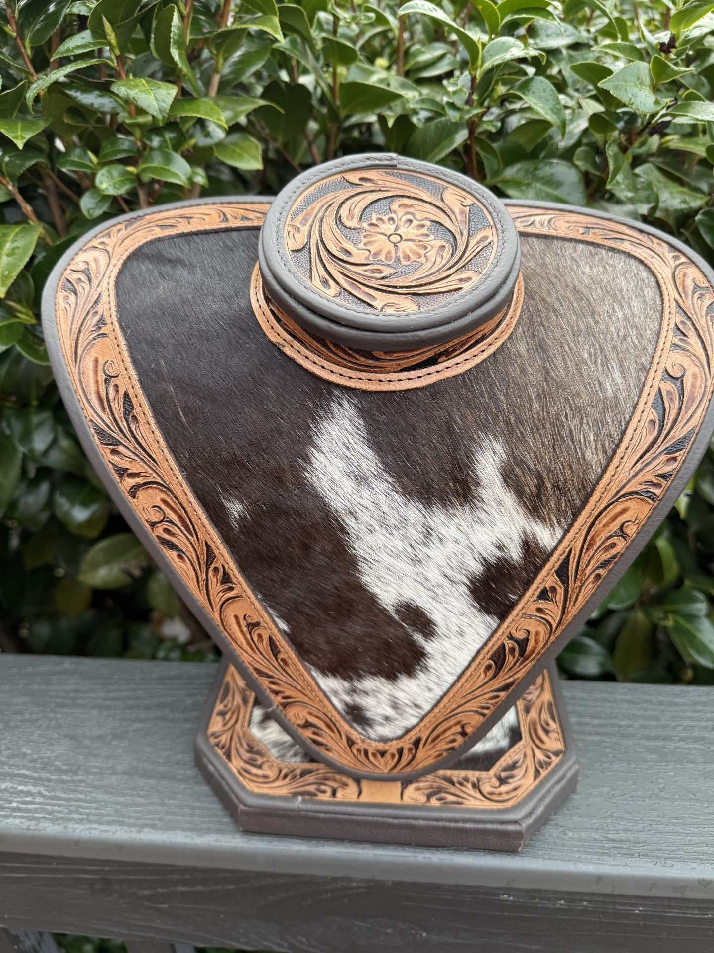 Necklace display with dark and light brown tooled leather and black and white cowhide pattern
