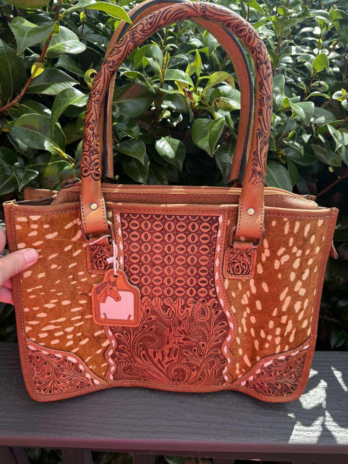 Deer tooled leather tote bag in tan cowhide with cream spots, reddish-brown carved floral panels and ornate handles