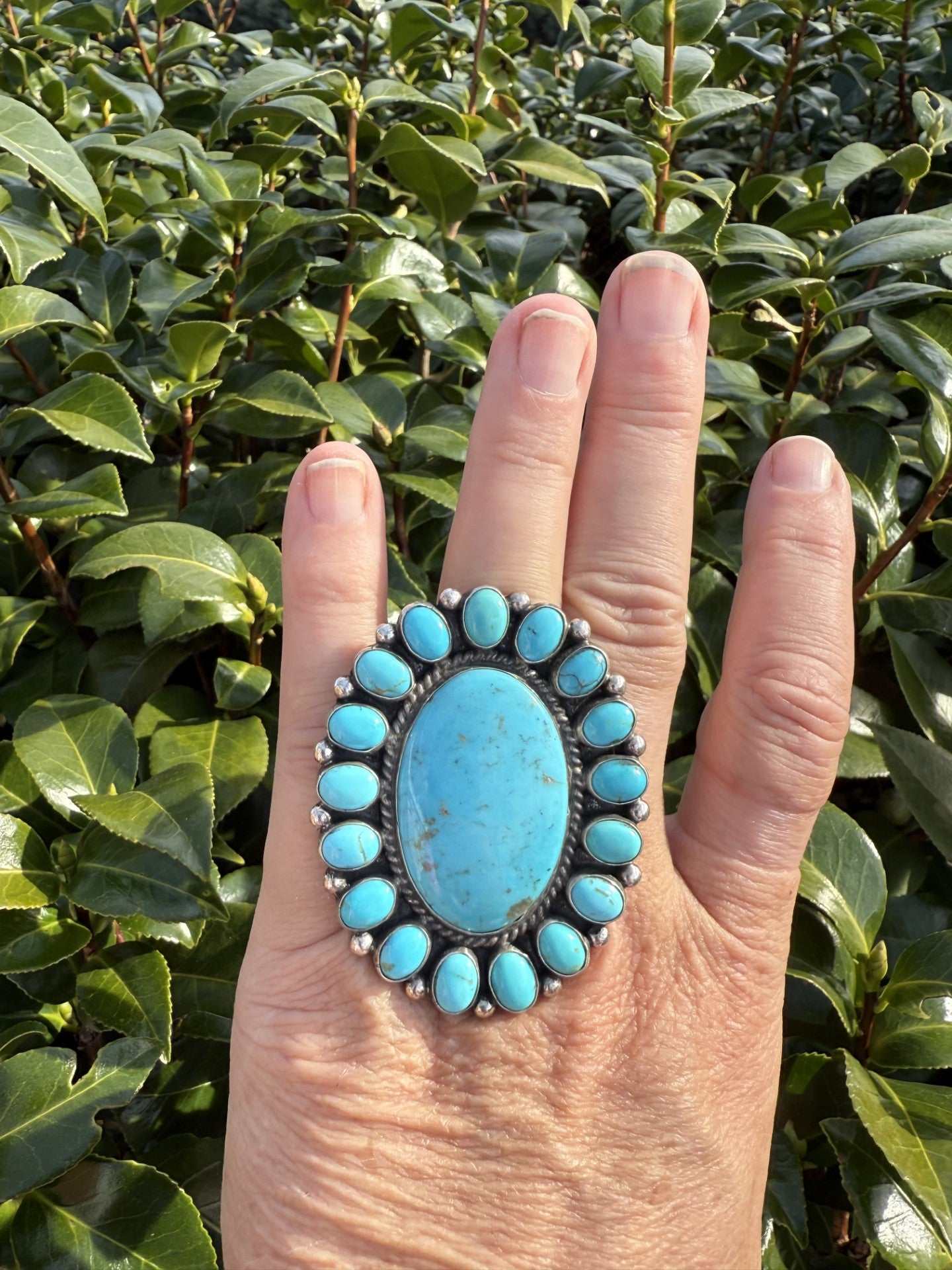 Kingman Turquoise Cluster Ring with large oval turquoise center and smaller stones in Navajo design by Devin Brown on hand outdoors