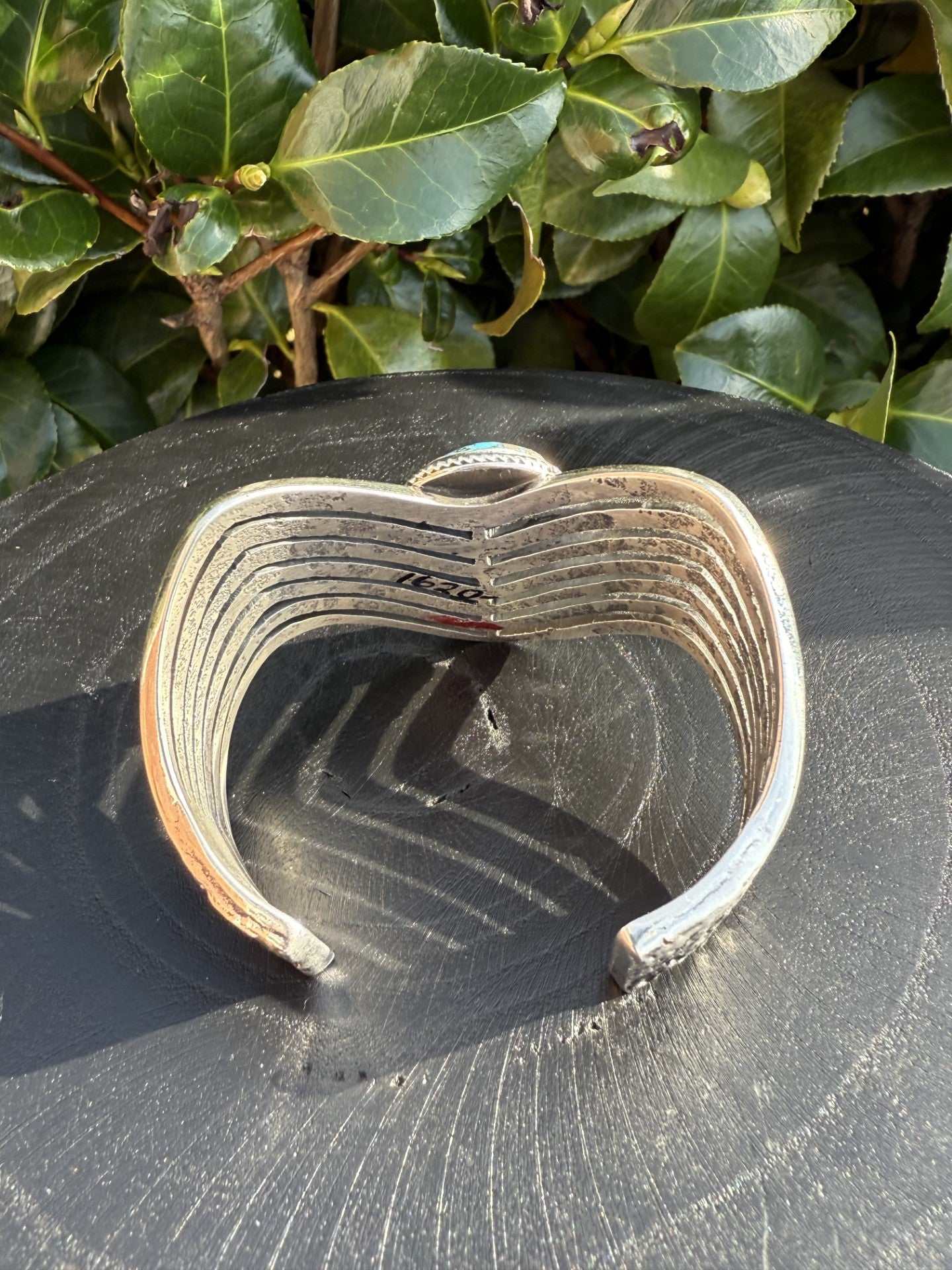 Navajo style Persian Turquoise Bracelet-cuff with pyrite by Aaron Anderson, displayed on black surface with greenery background