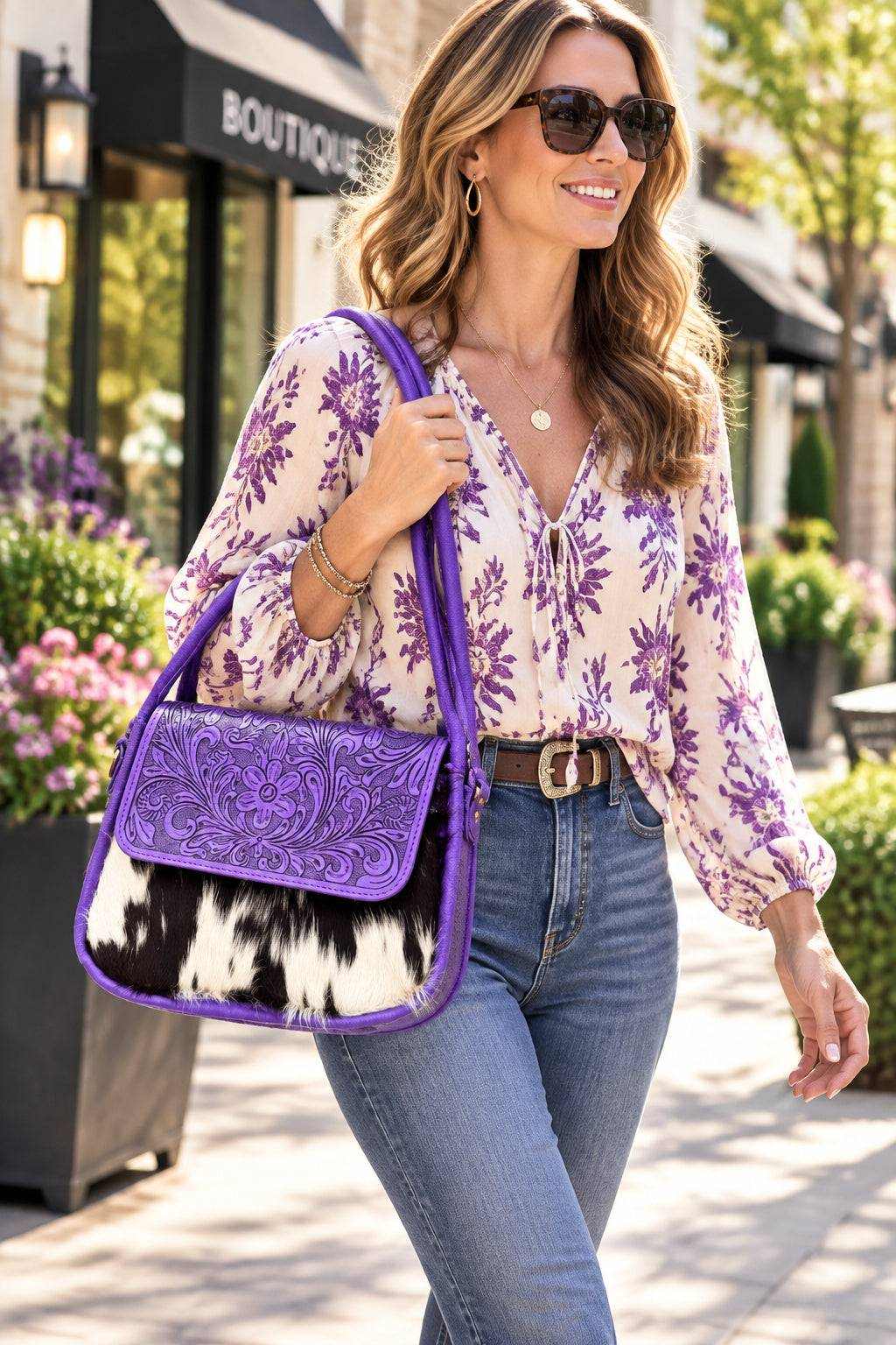 Purple tooled leather shoulder bag with ornate embossed scrollwork, bright purple trim and a black-and-white cowhide panel