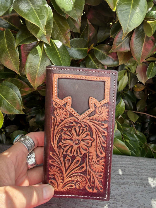 Tooled leather men’s wallet in dark brown leather with a raised floral design, orange-brown tooling and stitched edges