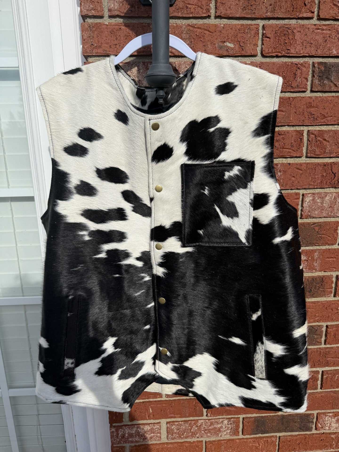 XL size cowhide men’s vest in black and white Western leather design hanging against red brick wall